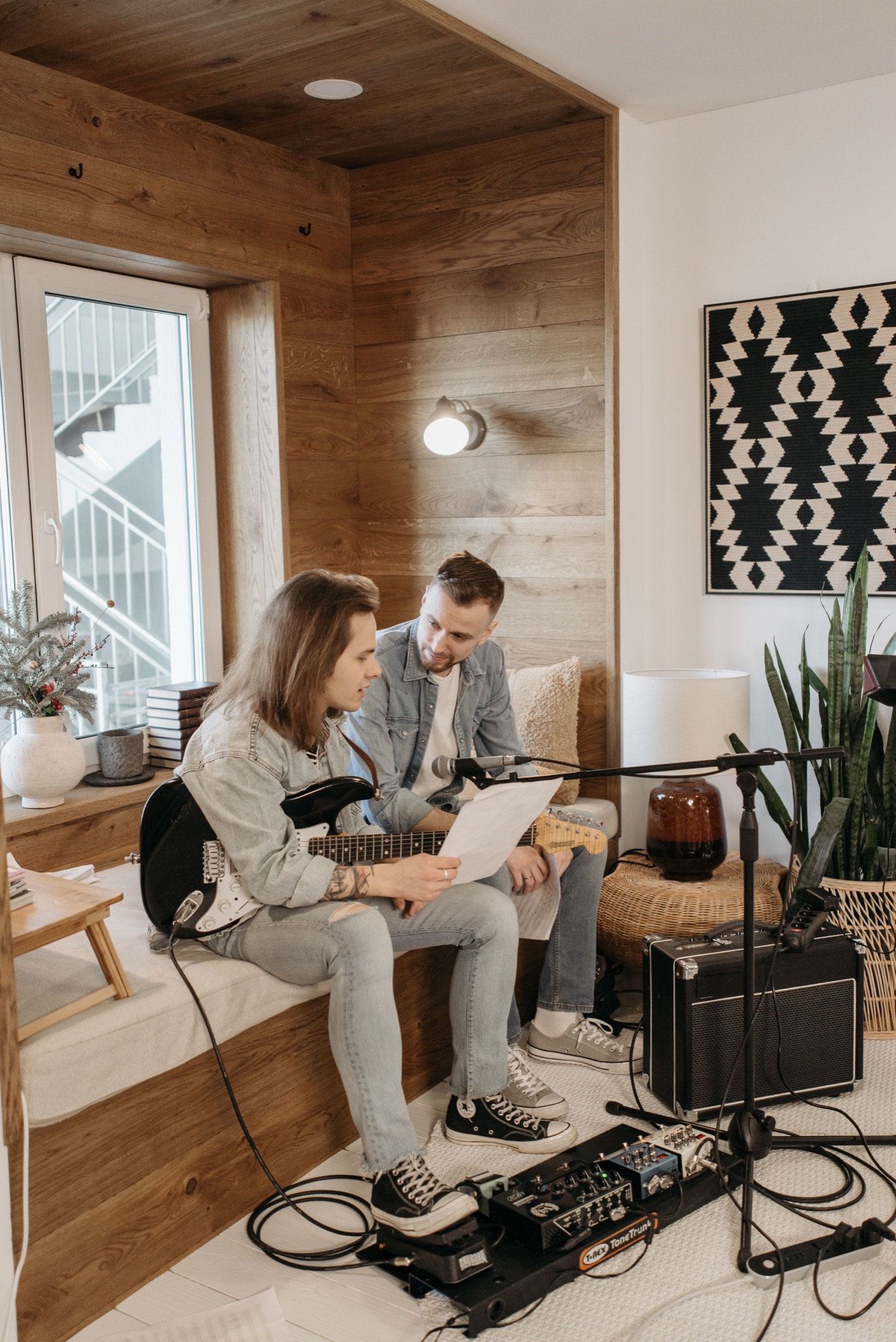 Two musicians writing with guitar and laptop in a warm home studio